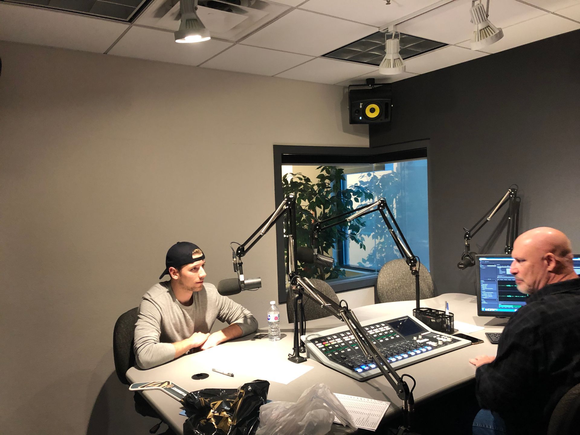 Two people seated in a recording studio, speaking into microphones at a radio console.
