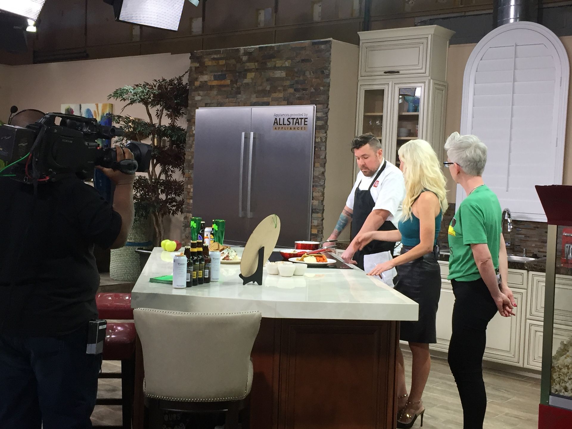 People cooking at a kitchen island with a camera crew filming in the background