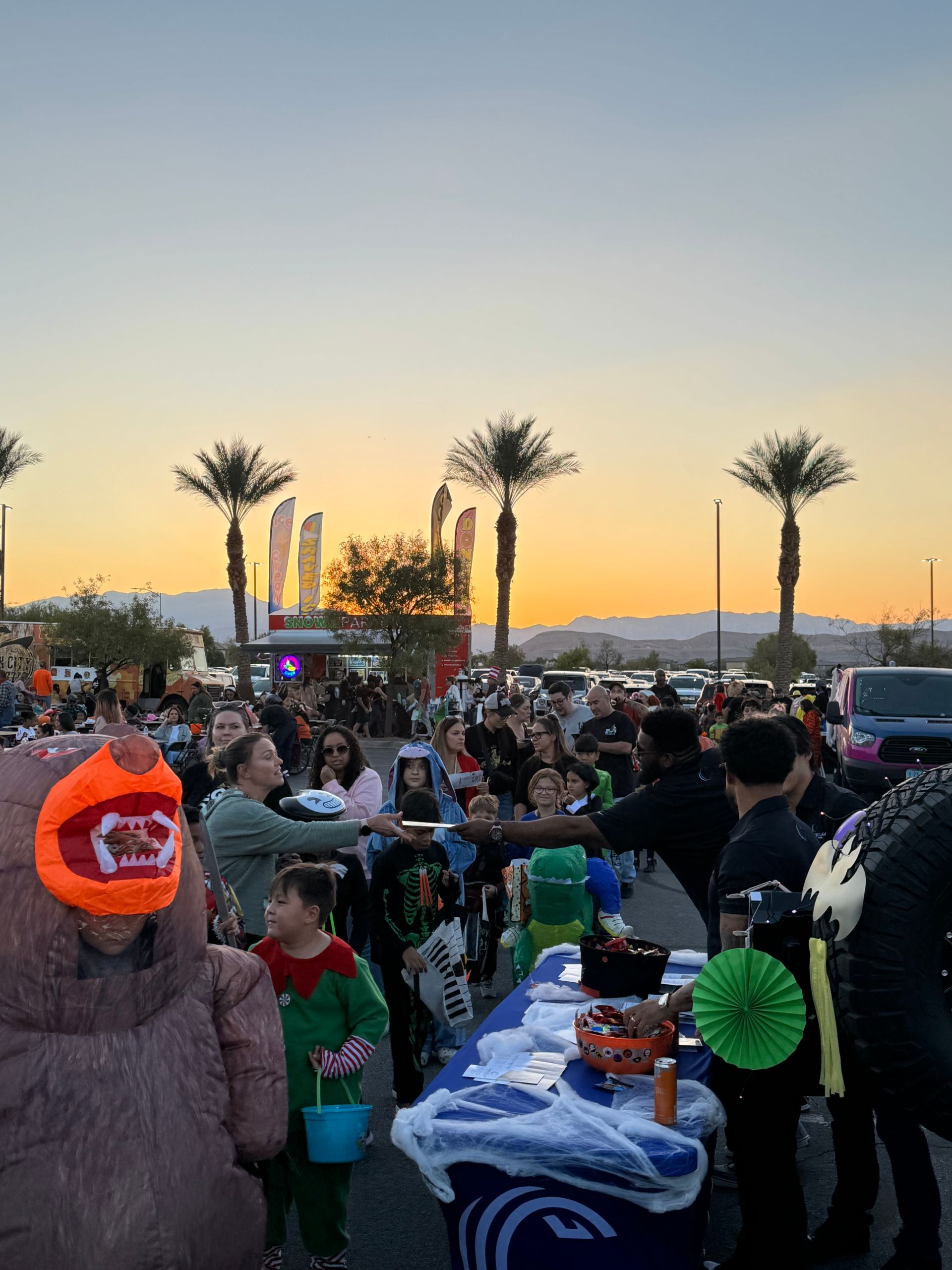 Crowd at an outdoor sunset gathering with palm trees and colorful decorations