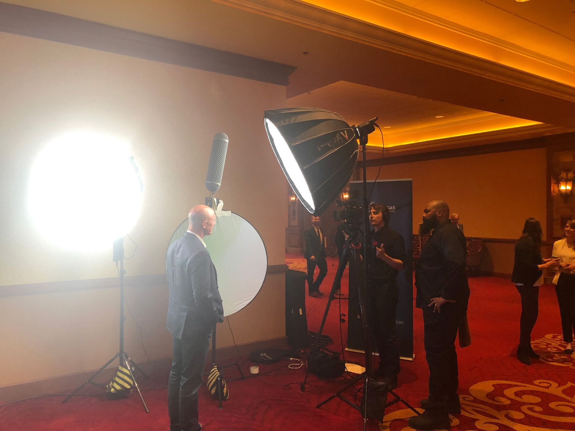 Man posing with camera lights and a large reflector at an indoor event venue