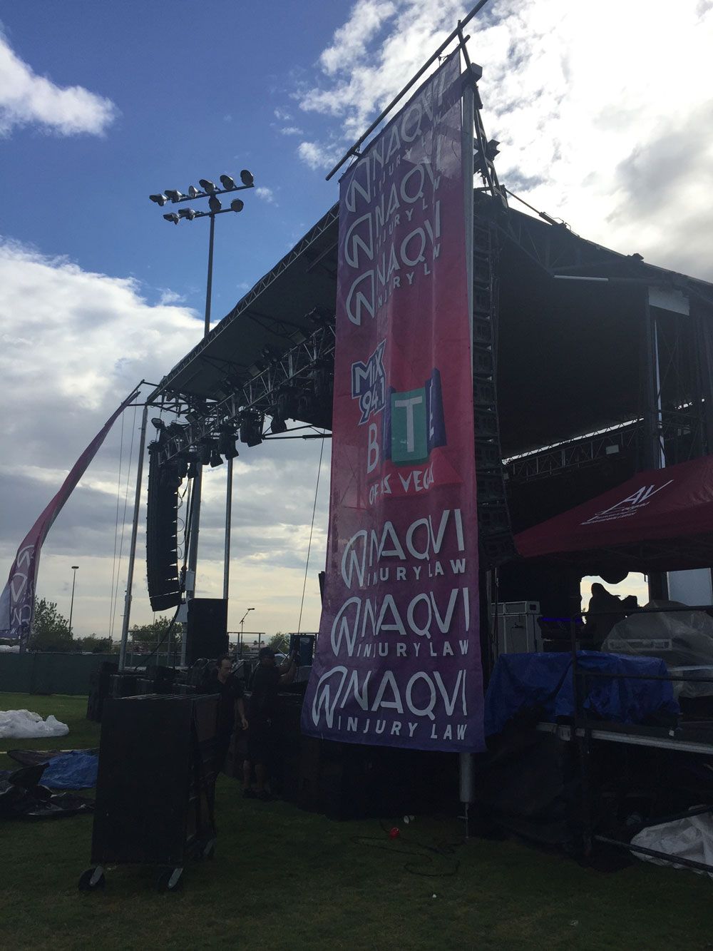 Outdoor concert stage with a tall purple banner, speakers, and cloudy sky at dusk