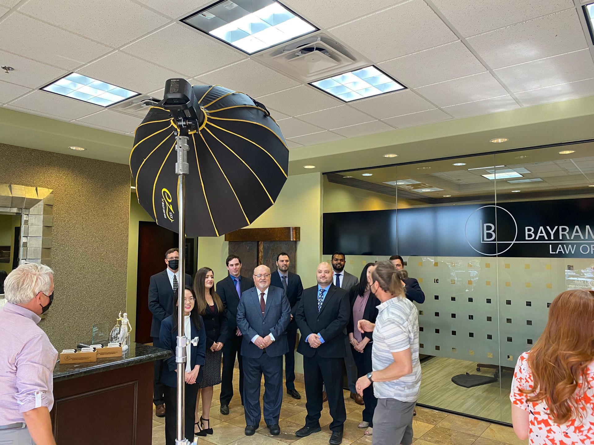 People standing in a lobby during a formal group photo beside a large studio light.