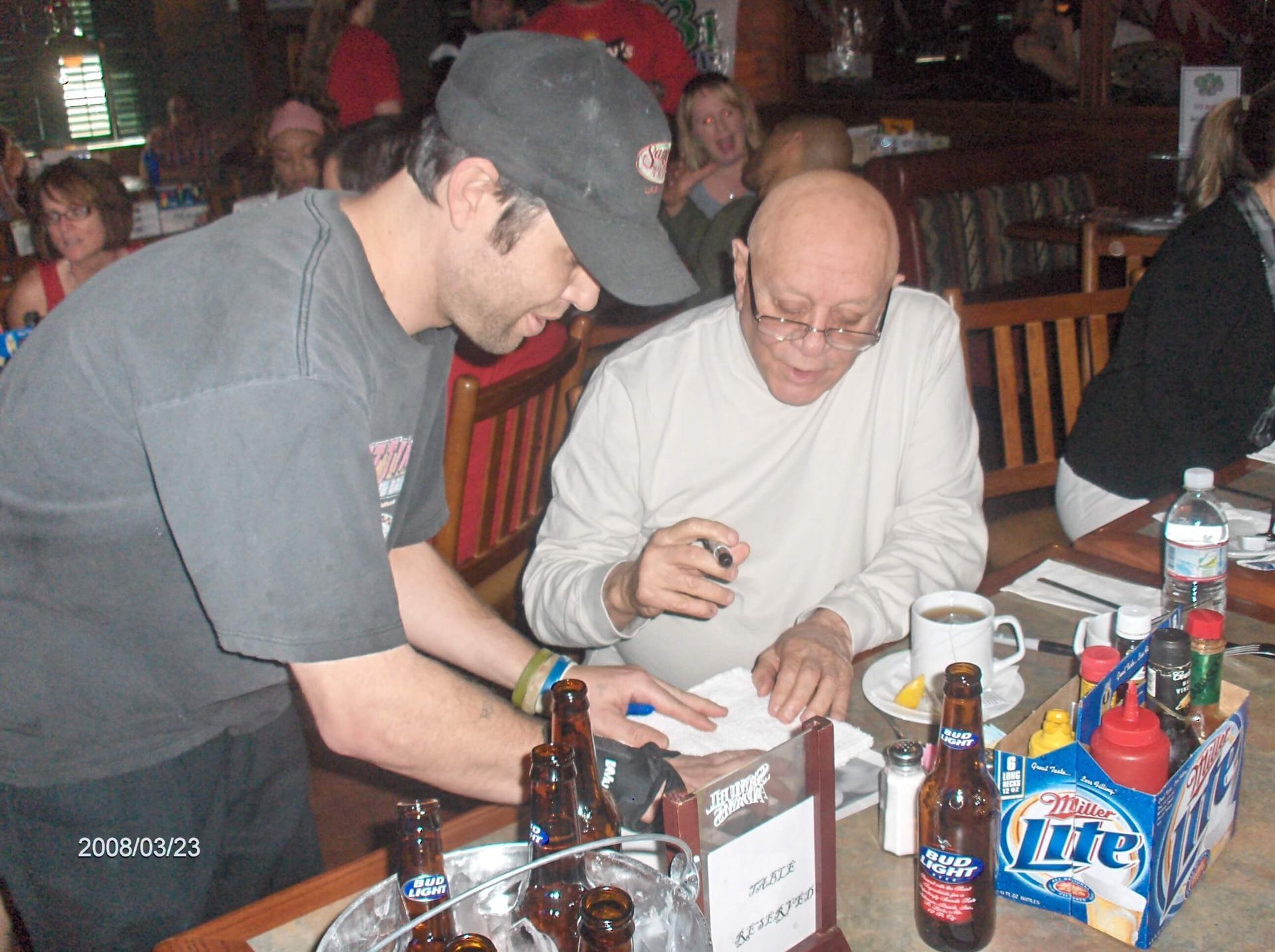 Two men leaning over papers at a restaurant table with drinks and condiments.