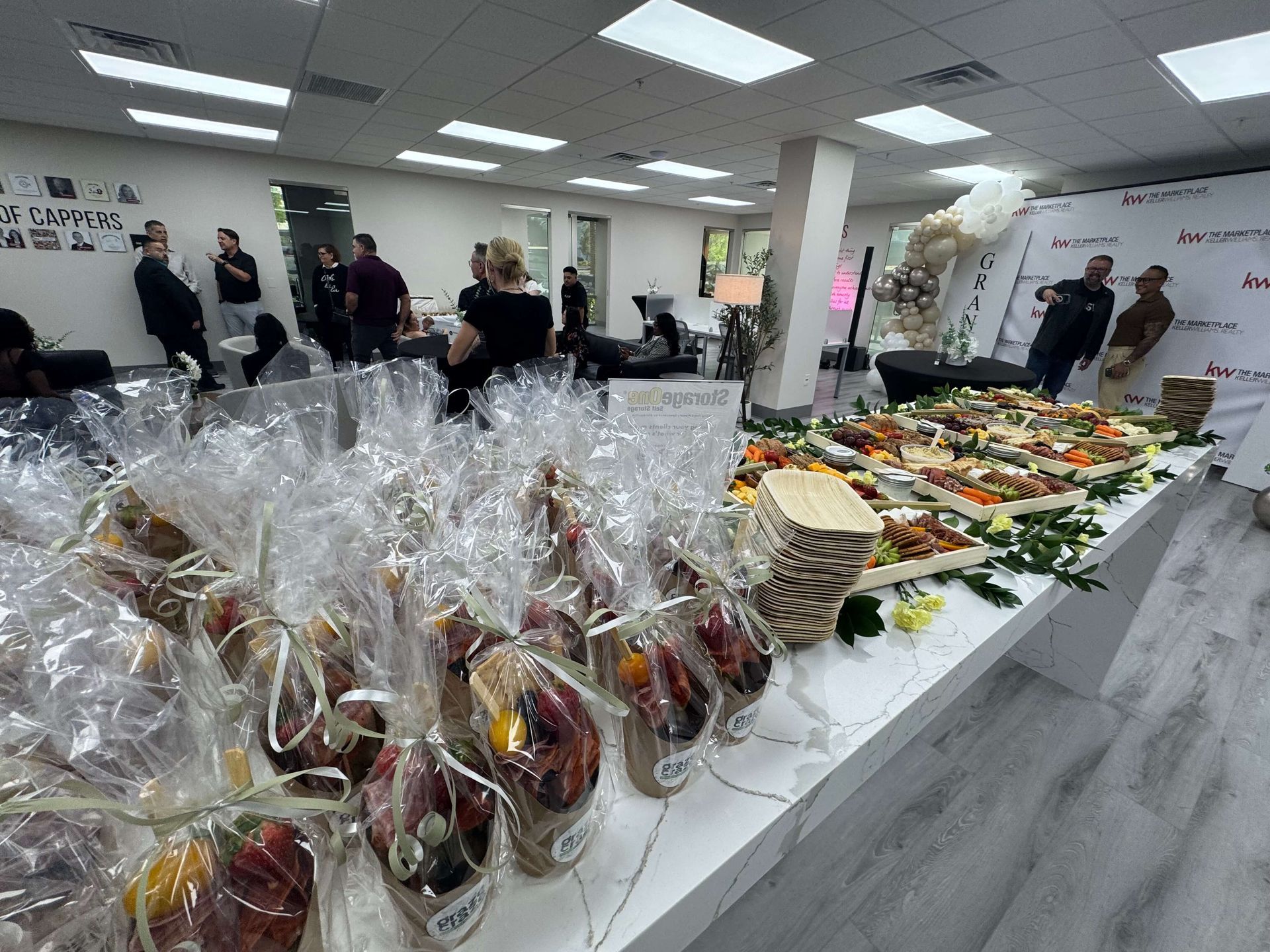 Buffet table with wrapped fruit baskets and trays of appetizers in a bright indoor event space