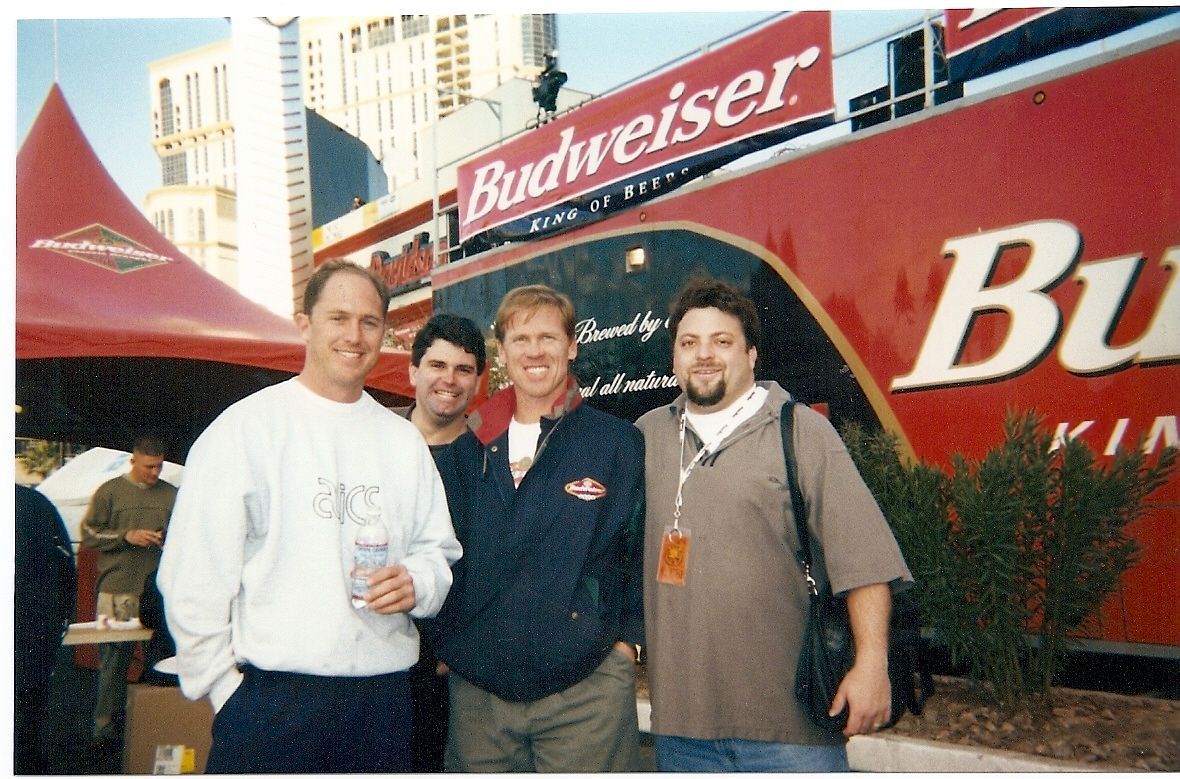 Four people posing in front of a red Budweiser trailer at an outdoor event