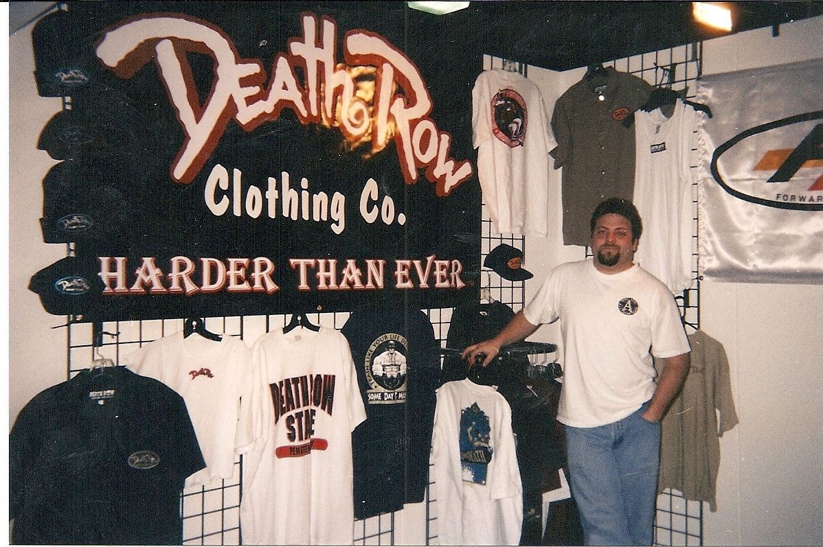 Death Row Clothing Co. display with hanging shirts and a man standing beside the “Harder Than Ever” sign