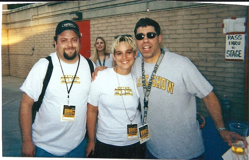 Three people posing together at an indoor event, wearing matching lanyards and casual shirts.
