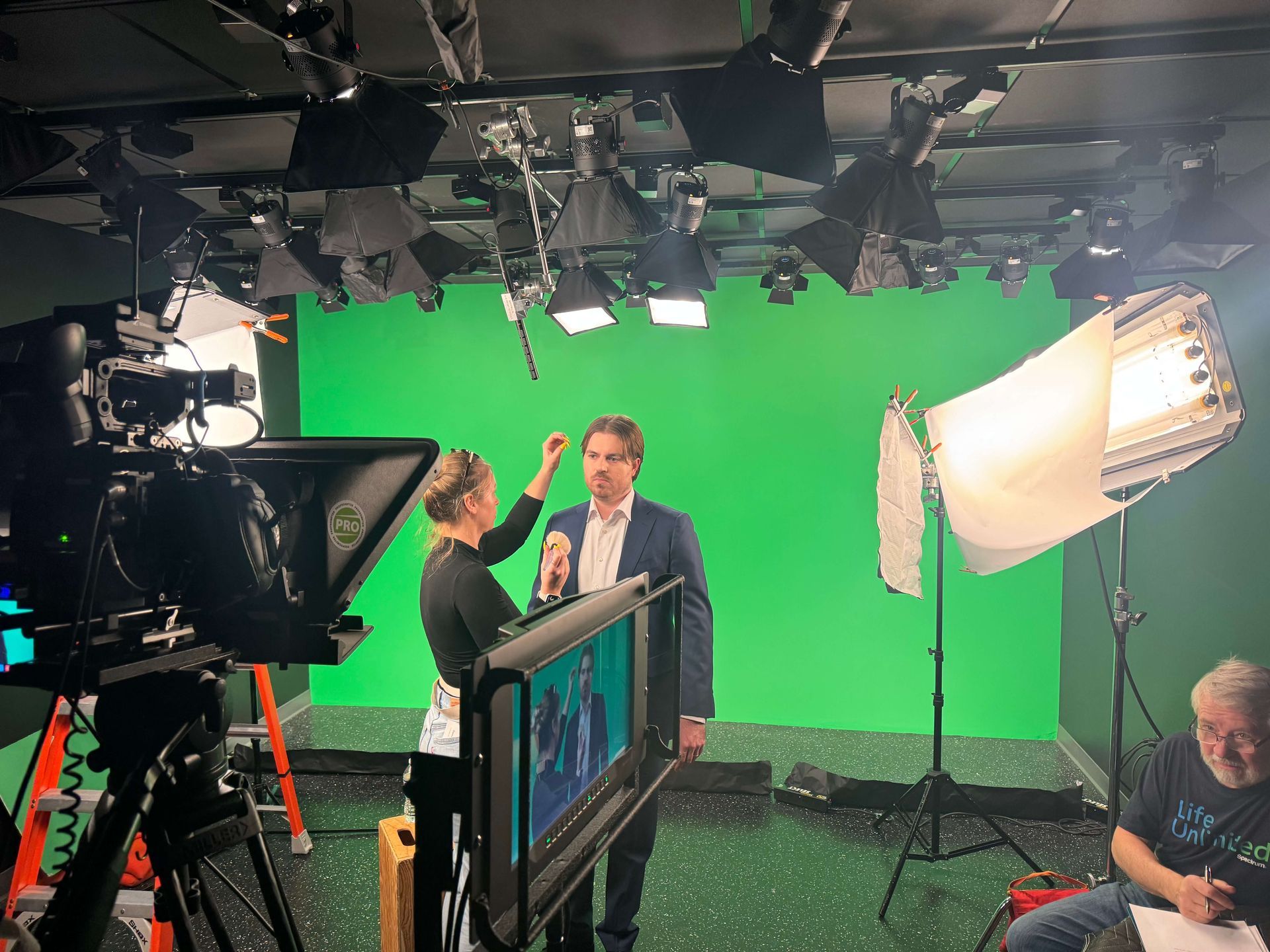 Film studio with green screen, cameras, lights, and two people posing for a shoot.
