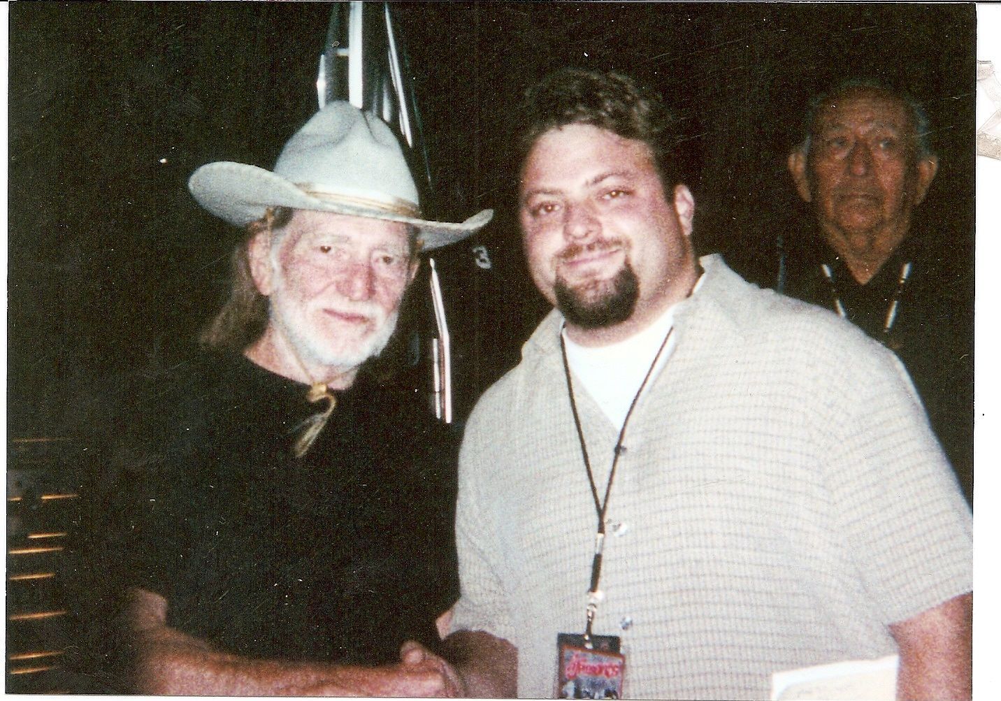 Two smiling men posing indoors, one in a white cowboy hat and the other wearing a lanyard.