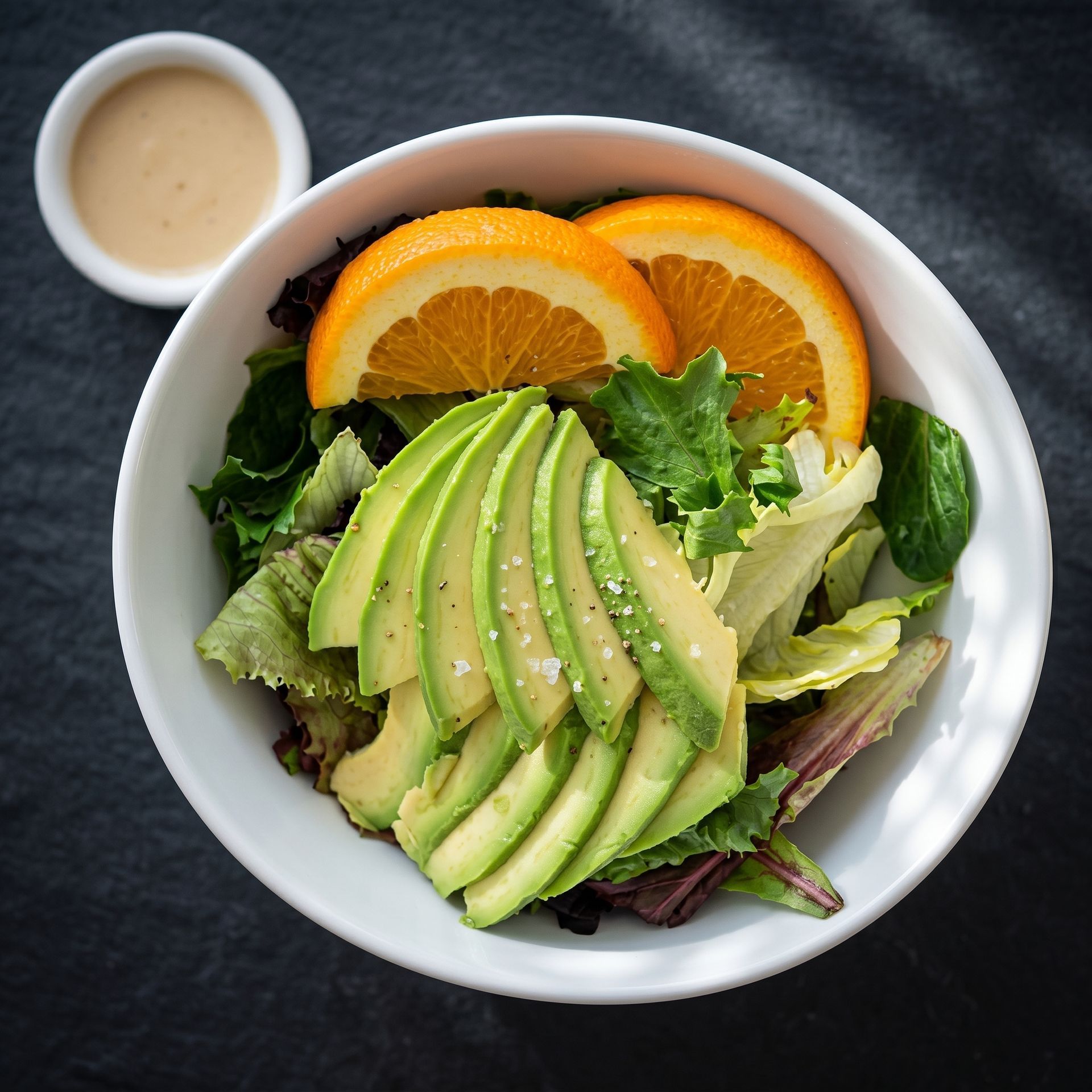 Avocado salad with orange slices in a white bowl, served with a small cup of dressing