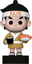 Cartoon sushi chef figurine in beige uniform, holding a sushi tray and a soy sauce cup on a black base.