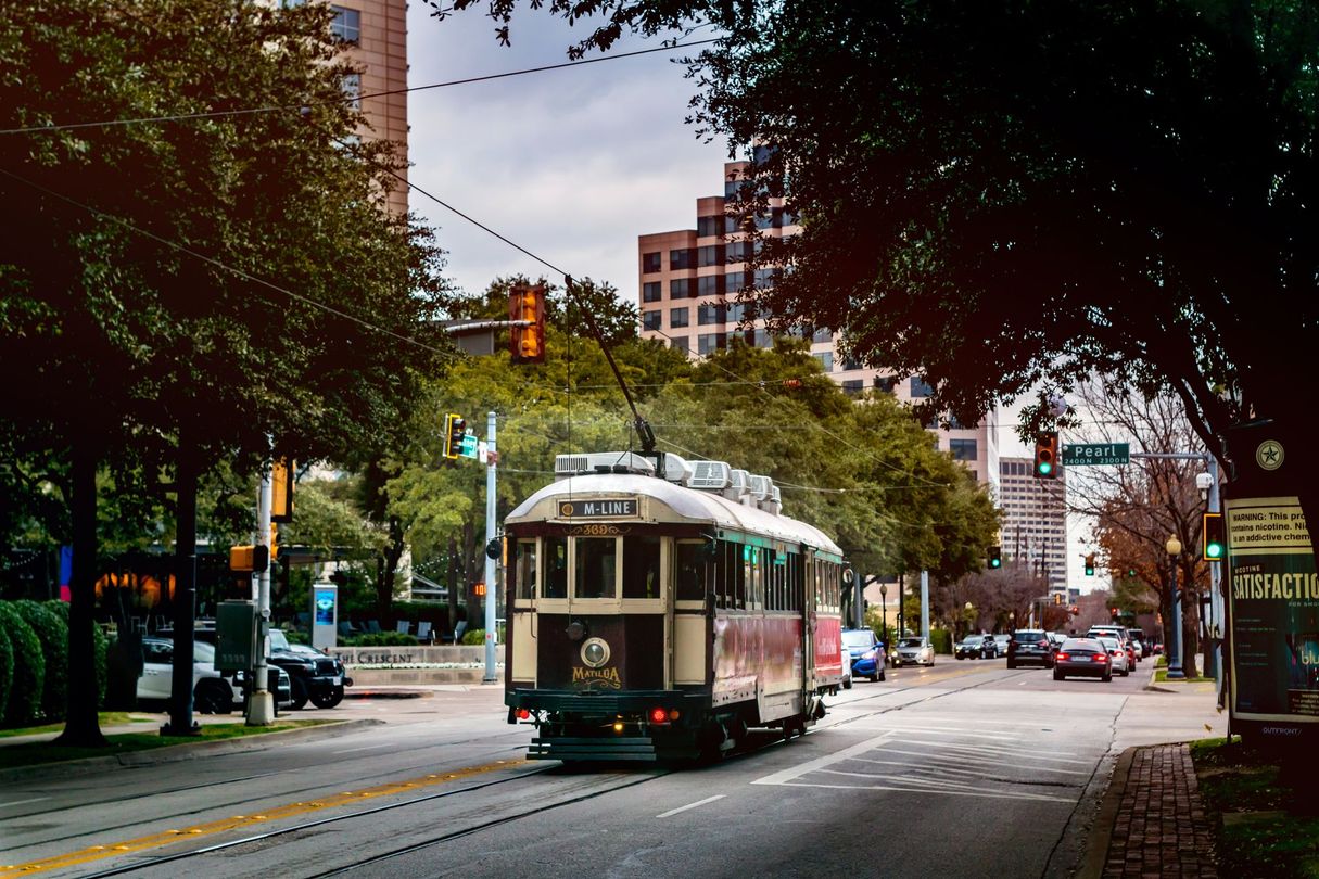Green streetcar on a tree-lined city street under an overcast sky, approaching an intersection