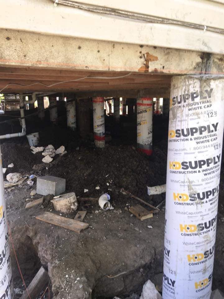 A construction site showing foundation piers and beams being installed for structural stability and repair