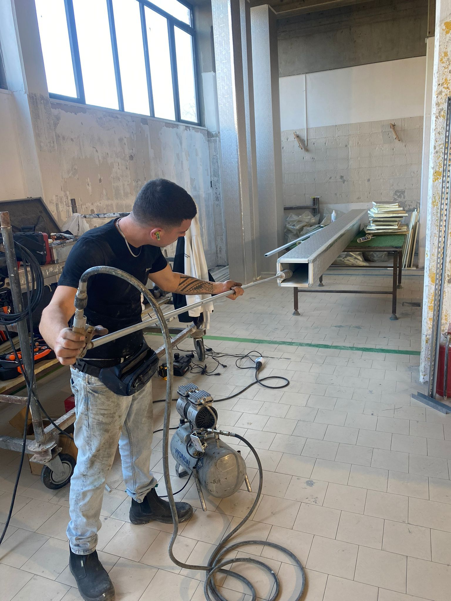 Un tecnico è chino su un macchinario in un'officina, intento a regolare i cavi accanto ad apparecchiature metalliche.