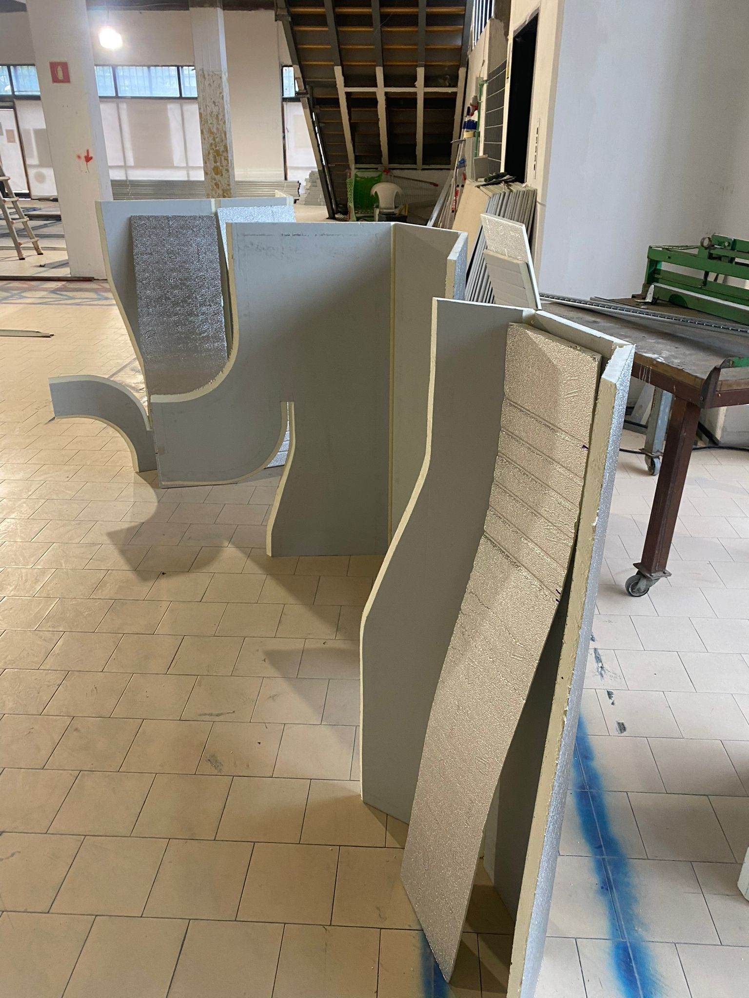 Pannelli di polistirolo impolverati allineati in un'officina, con un tavolo e materiali da costruzione nelle vicinanze.