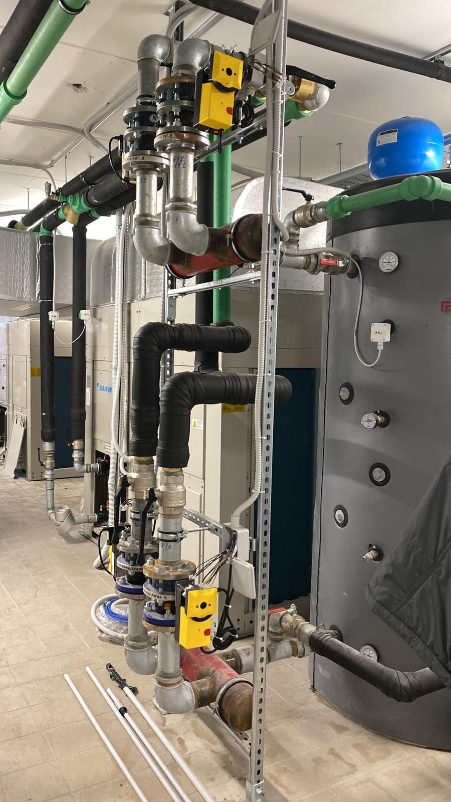 Tubazioni e valvole industriali accanto a un serbatoio grigio in un locale tecnico.
