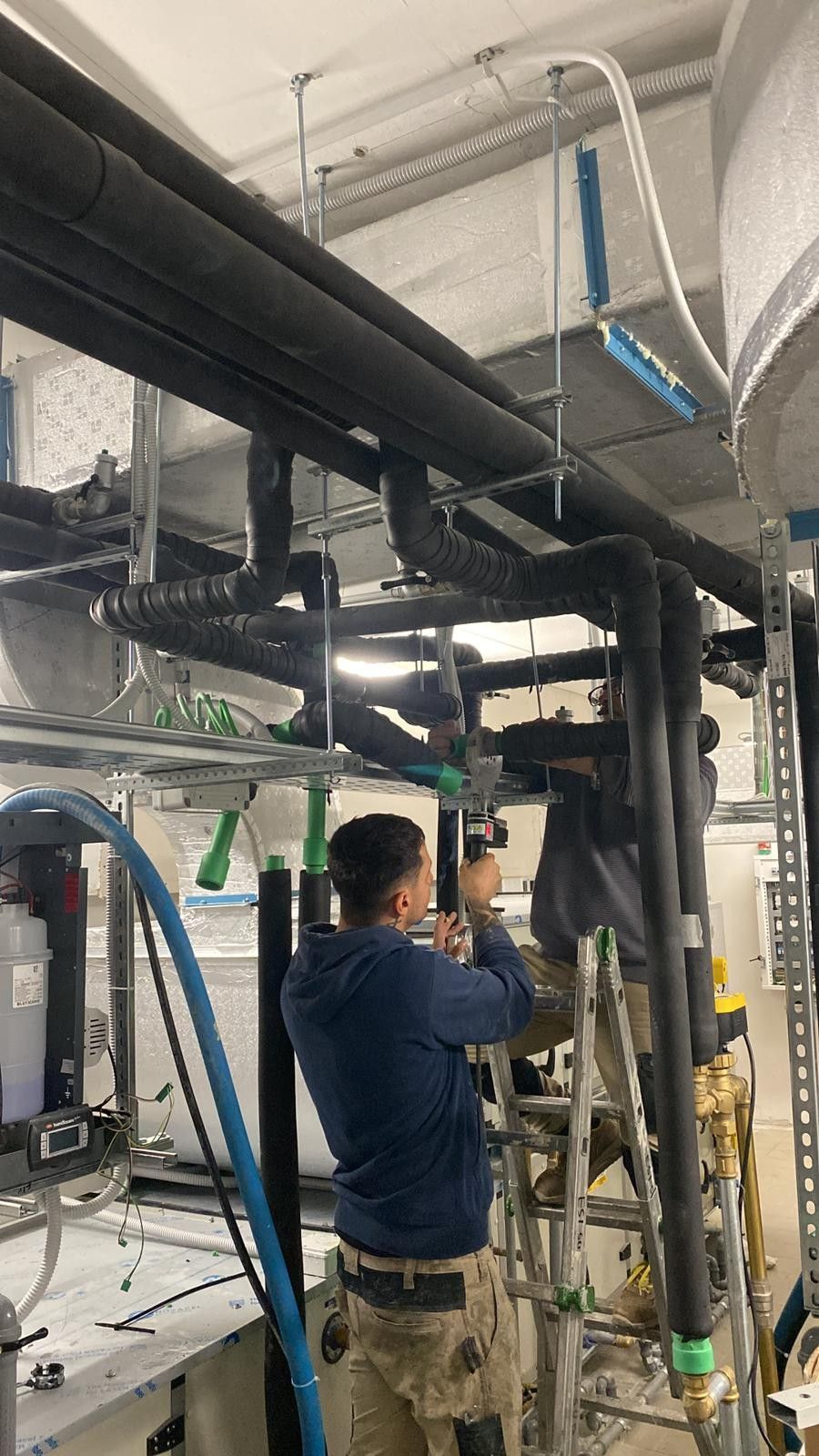 Un operaio ispeziona le tubature aeree in un locale tecnico industriale.