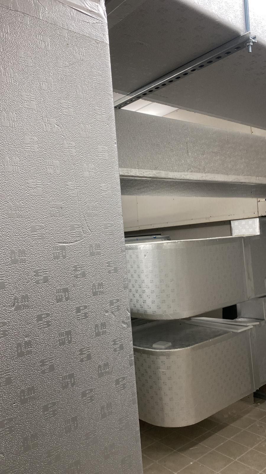 Primo piano di isolamento grigio screziato e condotti metallici all'interno del soffitto di un edificio.