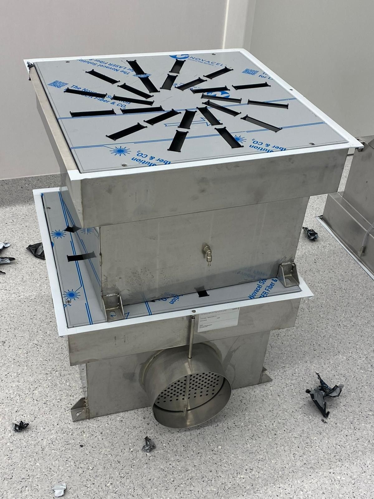 Ventilatore da tetto in metallo con alloggiamento quadrato argentato e griglia circolare su una superficie del tetto grigia.