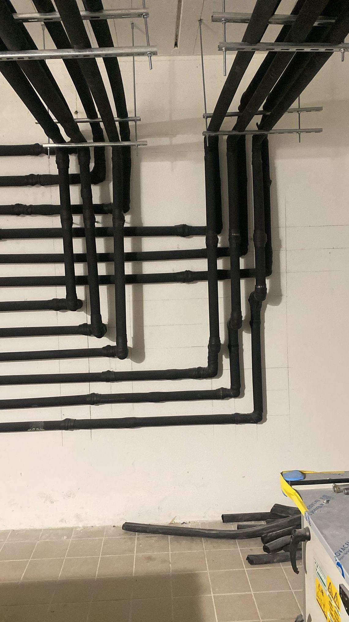 In un locale tecnico in fase di ristrutturazione, dei condotti per cavi neri corrono lungo una parete e un soffitto bianchi.