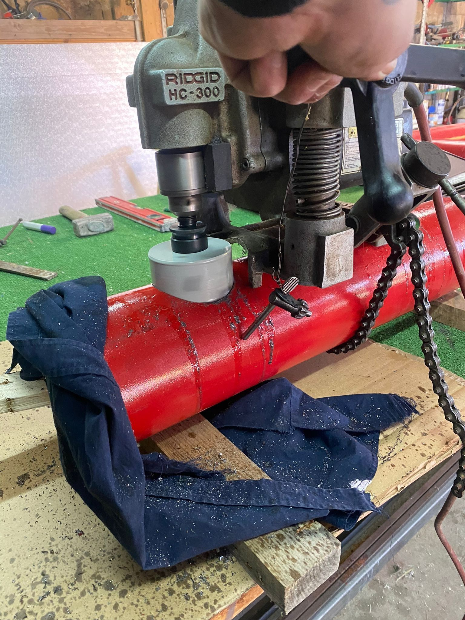 Mani che usano una pressa su un oggetto cilindrico rosso su un banco da lavoro con teli blu intorno.