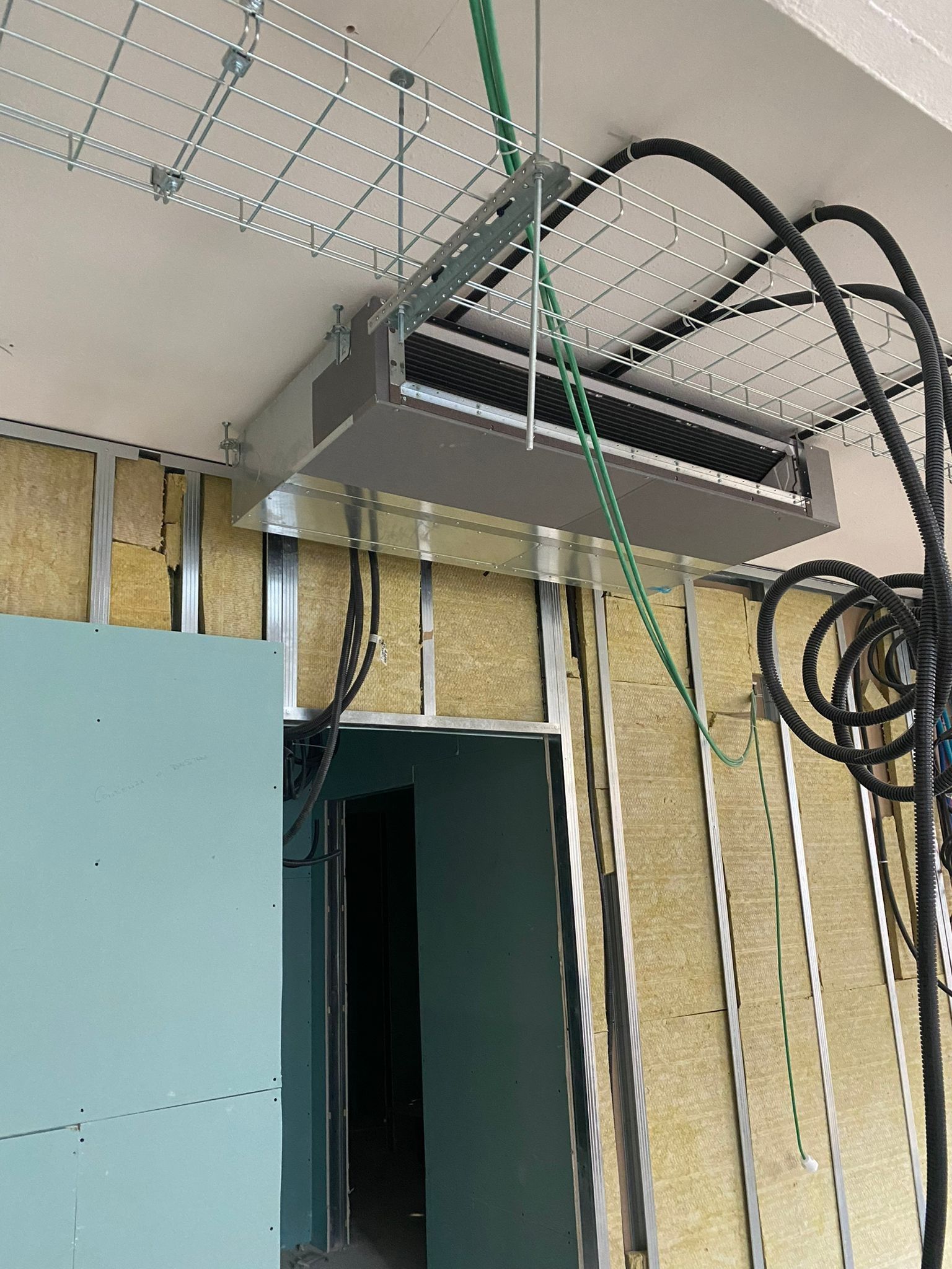 Apparecchiature di rete montate a soffitto e cavi raggruppati sopra una porta in una stanza in costruzione.