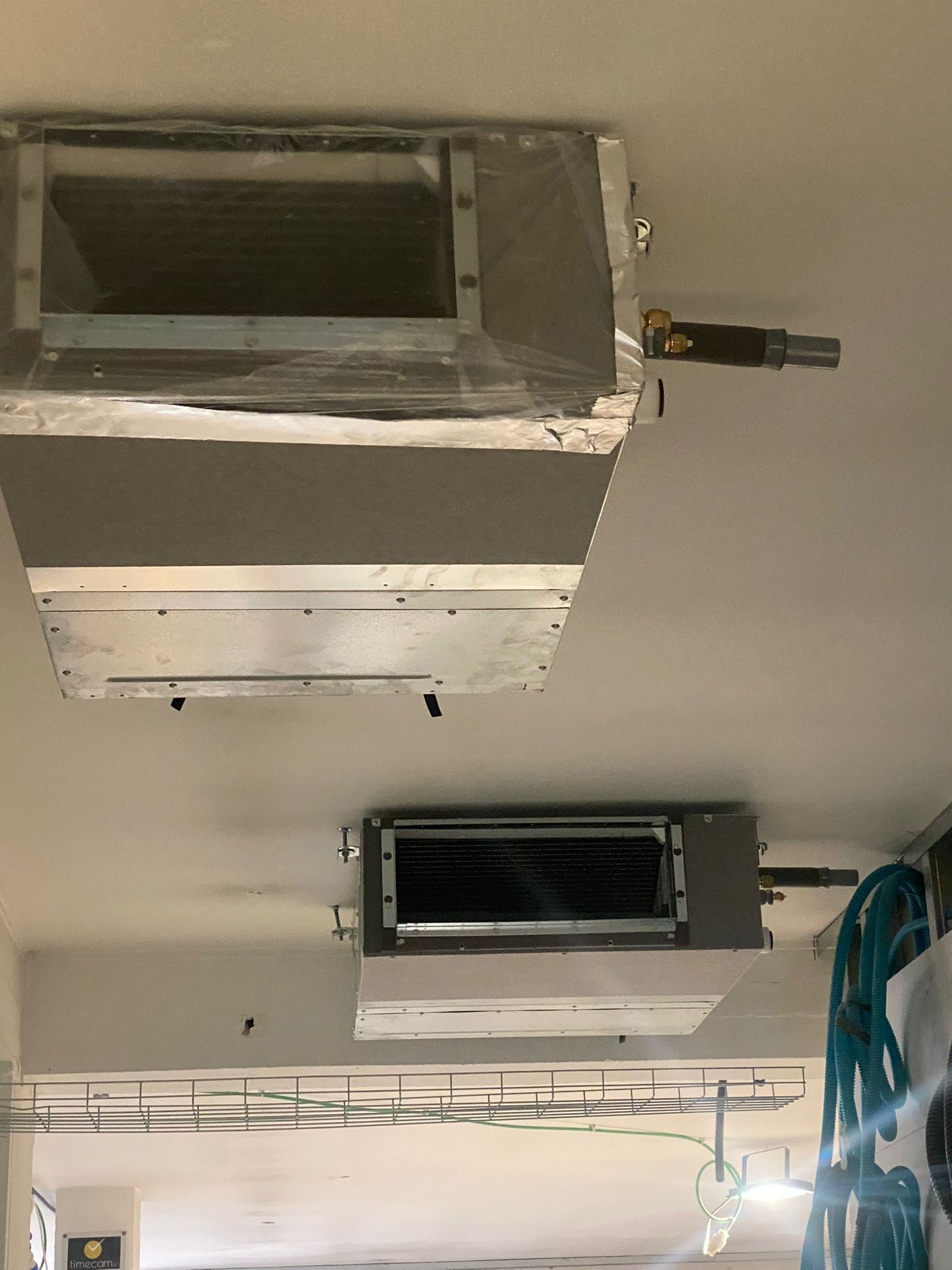 Soffitto con bocchette e condotti di ventilazione a vista in un'area di lavoro; cavi blu pendono sulla destra.