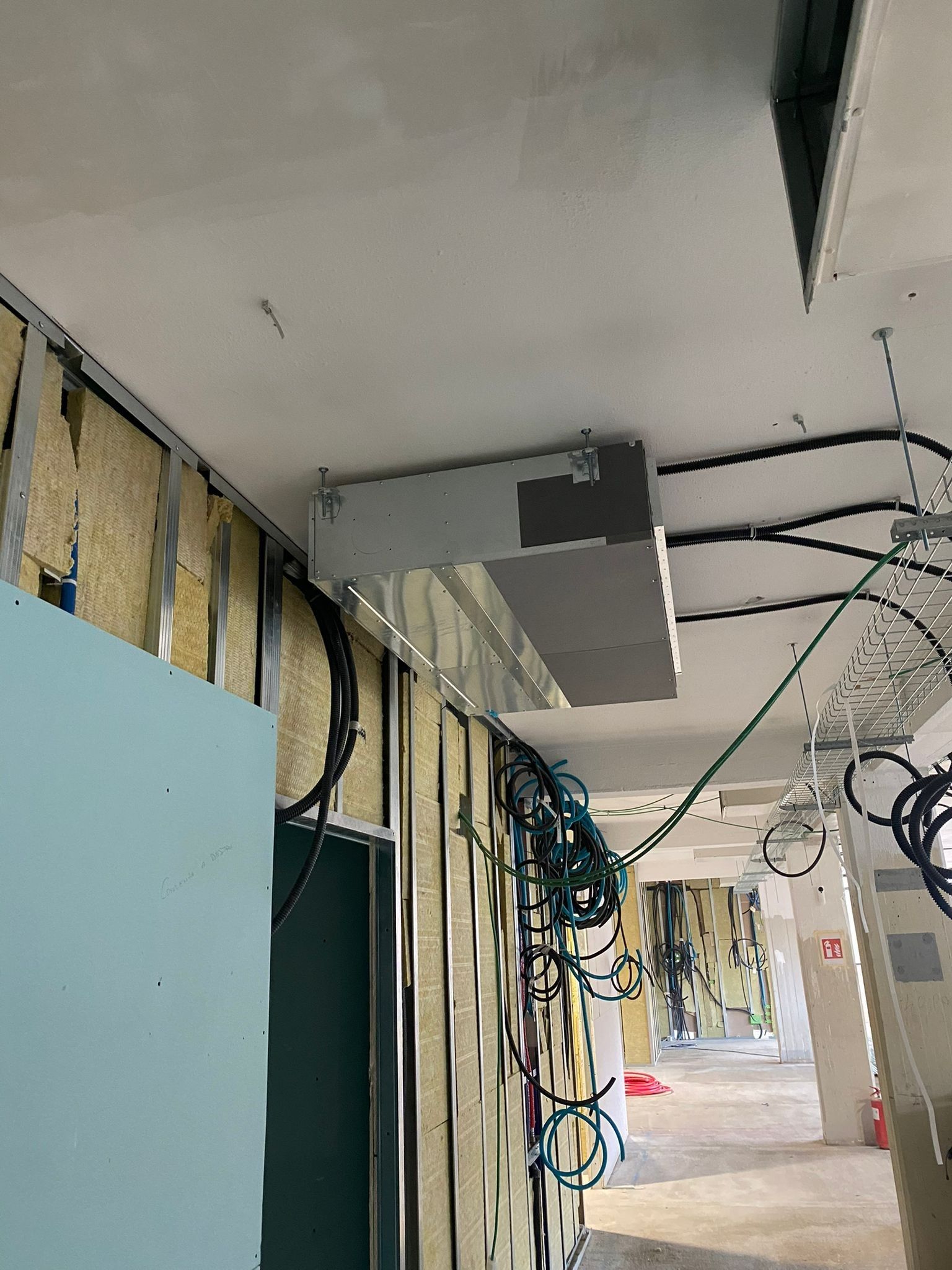 Cablaggio a vista sul soffitto di un corridoio commerciale in fase di ristrutturazione, con condotti e cavi sospesi in aria.