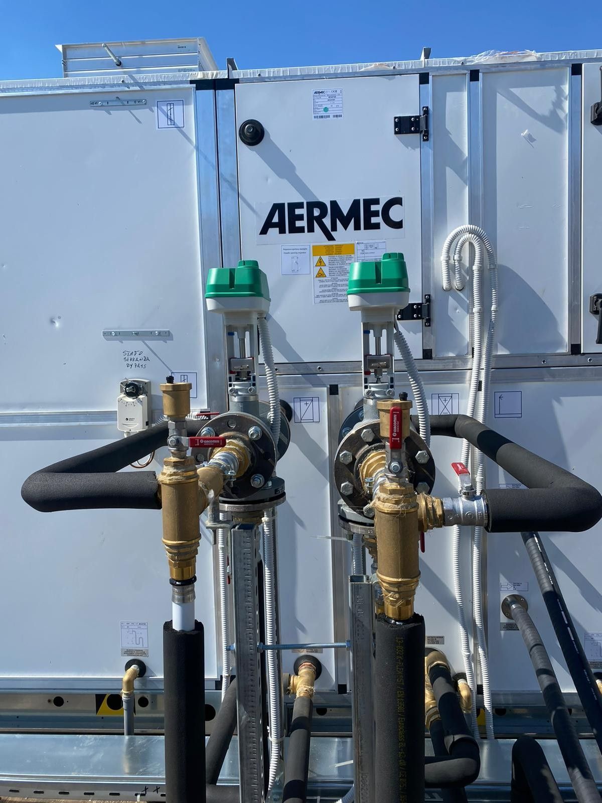 Unità HVAC da tetto AERMEC con tubi, valvole e tubi flessibili isolati contro un cielo limpido