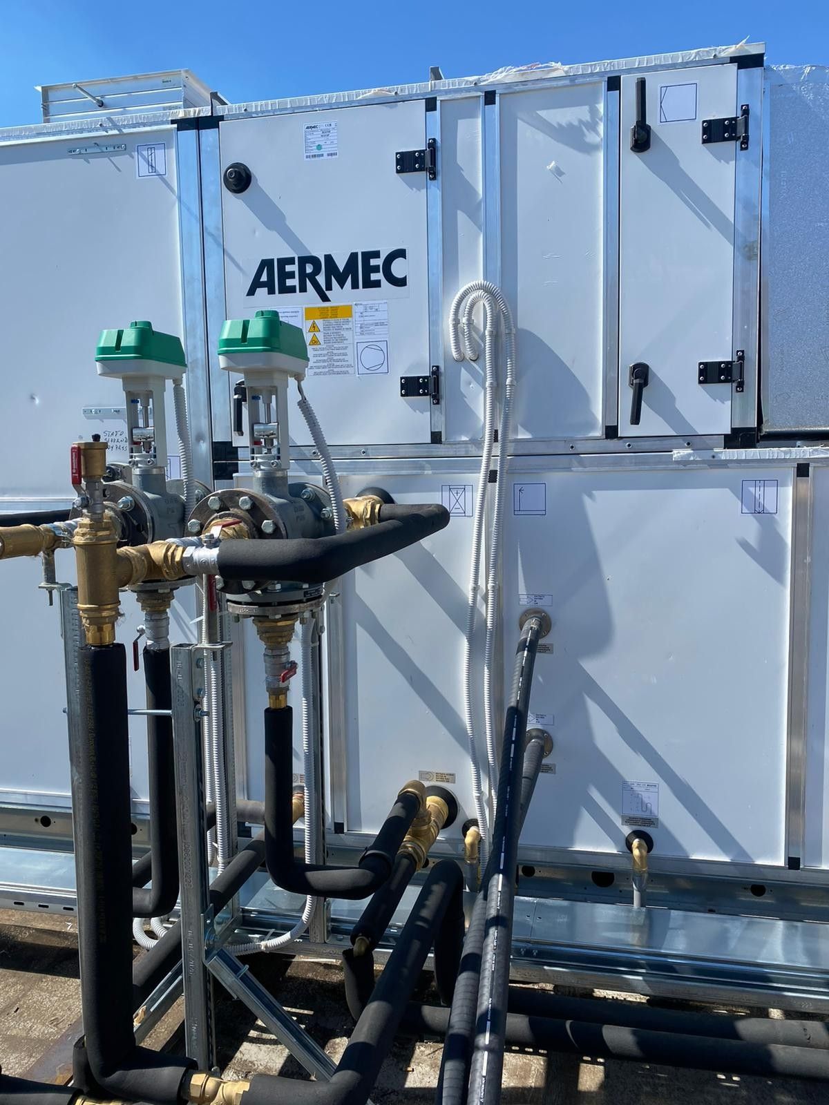Apparecchiature HVAC AERMEC con tubi e valvole su un tetto sotto un cielo sereno.