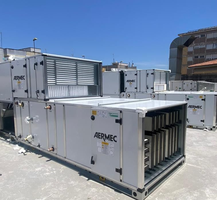 Grandi unità di climatizzazione Aermec di colore bianco installate sul tetto soleggiato di un edificio.