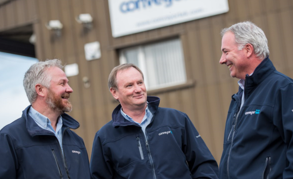 Three men are standing in front of a building talking to each other.