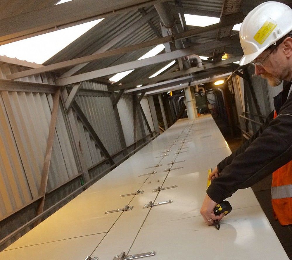 A man wearing a hard hat is measuring a conveyor