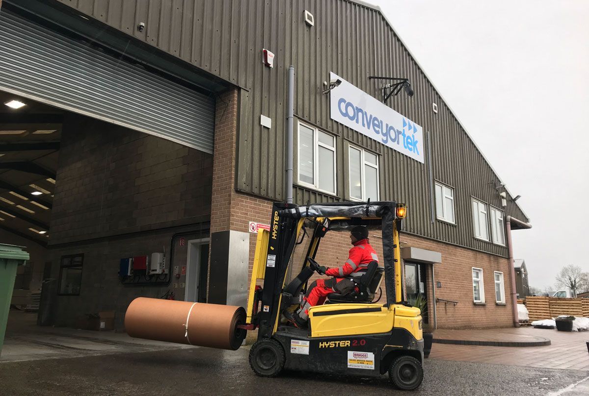 A man is driving a forklift in front of a Conveyor Tek building.