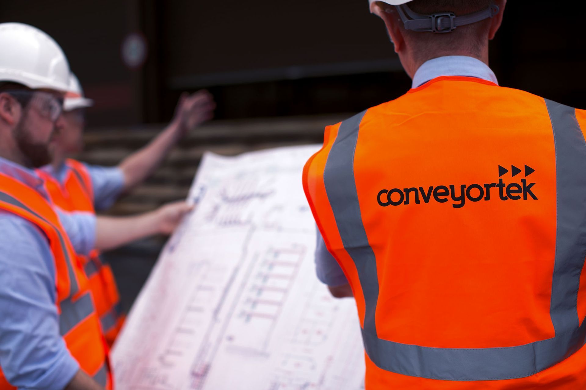 A man wearing a white hat and orange vest that says conveyortek