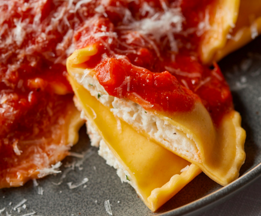 A plate of ricotta-filled ravioli topped with red marinara sauce and a dusting of grated cheese.