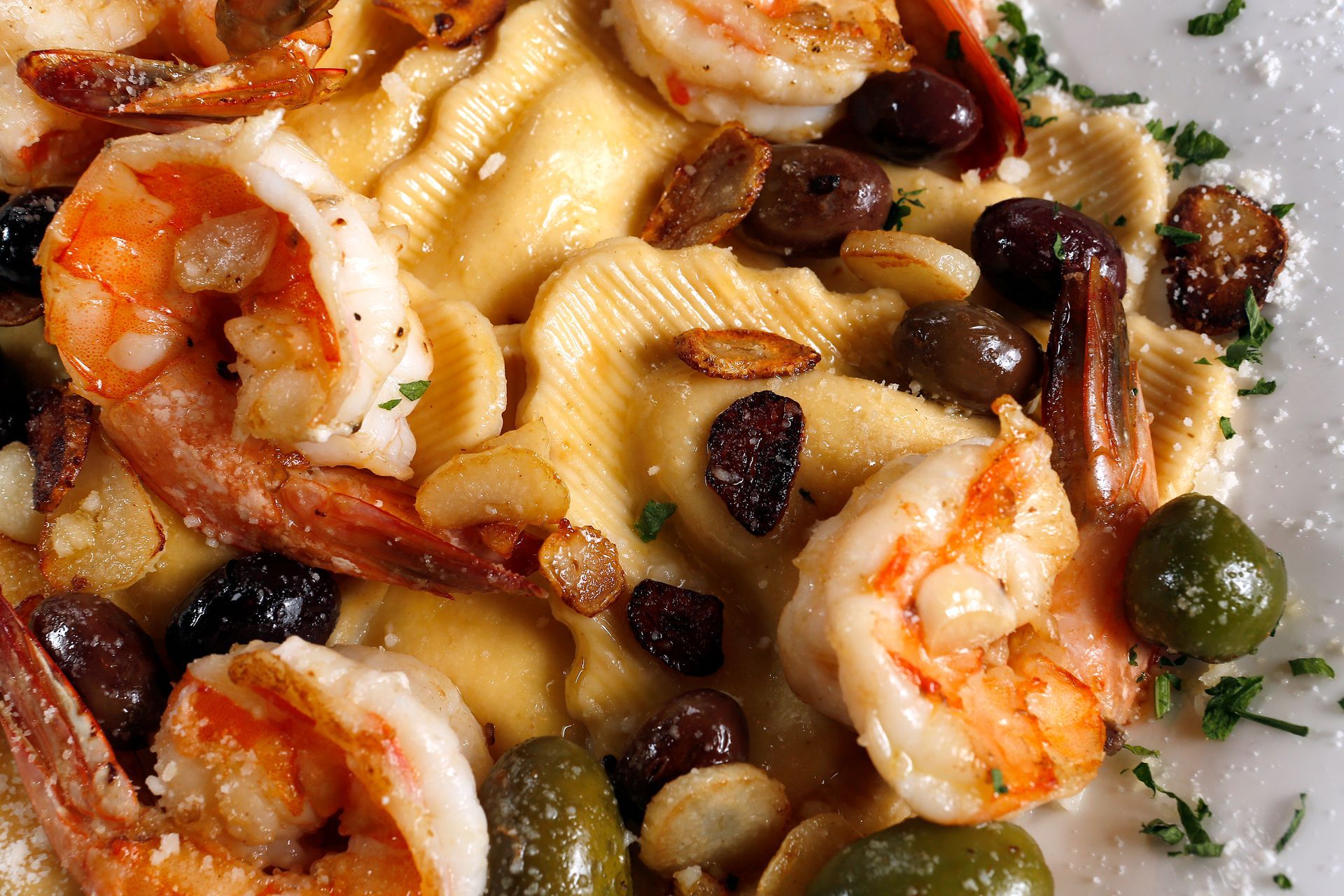 Shrimp pasta with olives and herbs on a white plate.