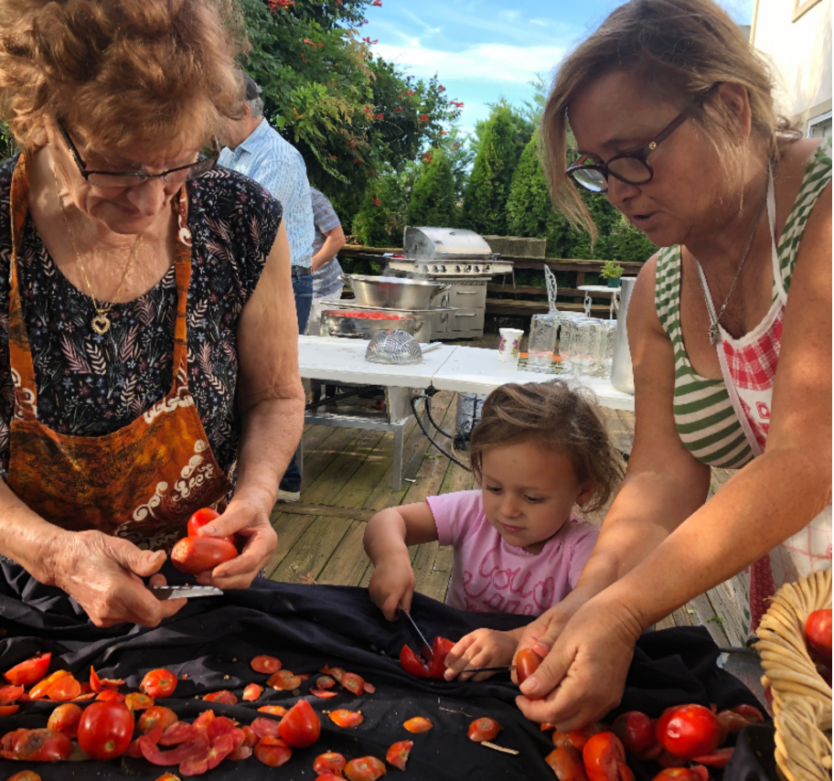 Two people and a young child preparing tomatoes together on a deck table covered with a black cloth.