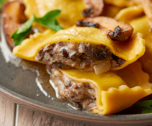 A close-up of mushroom-filled ravioli with herbs and a light sauce on a dark plate.