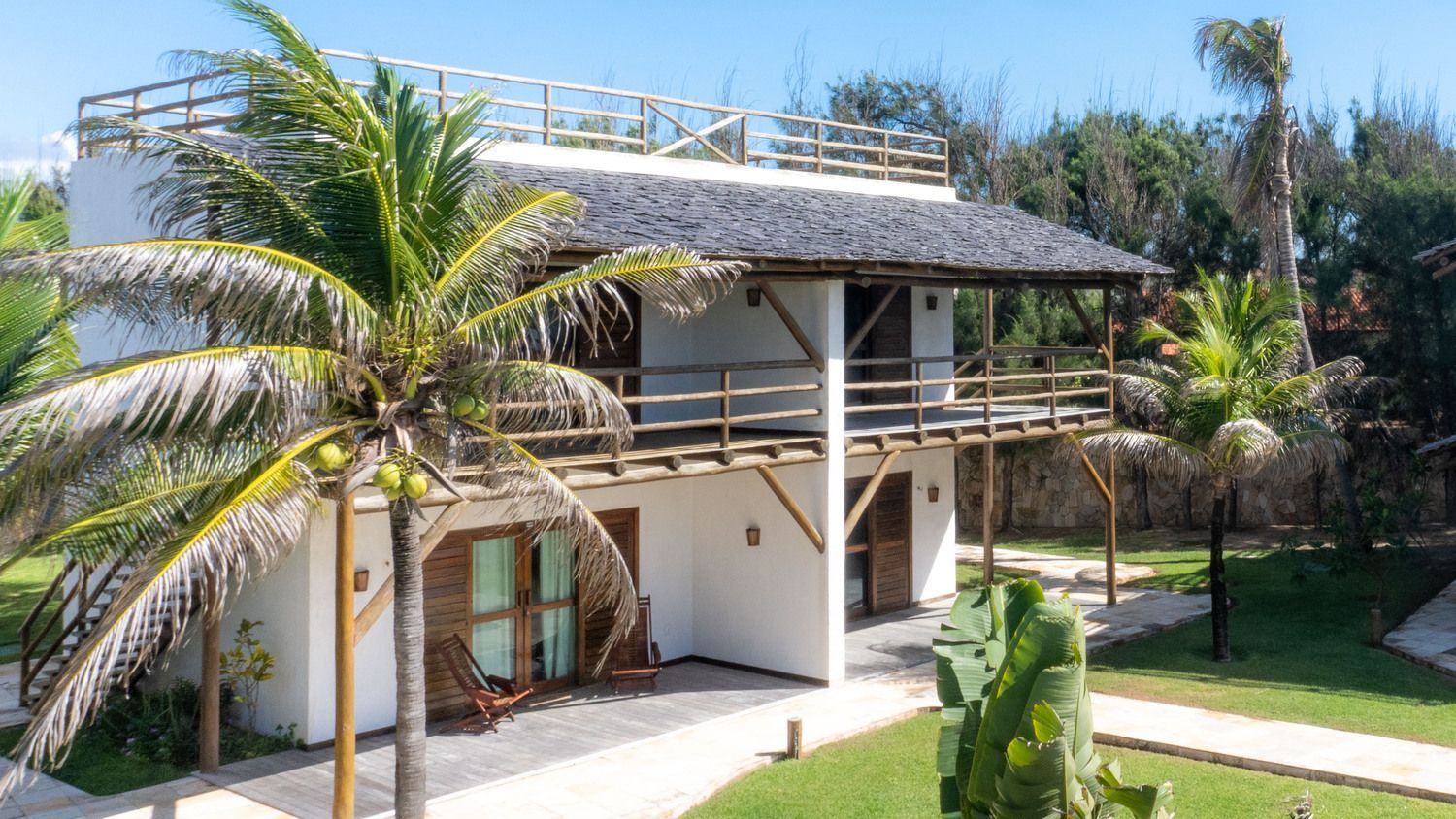 Uma grande casa branca com telhado de palha cercada por palmeiras.