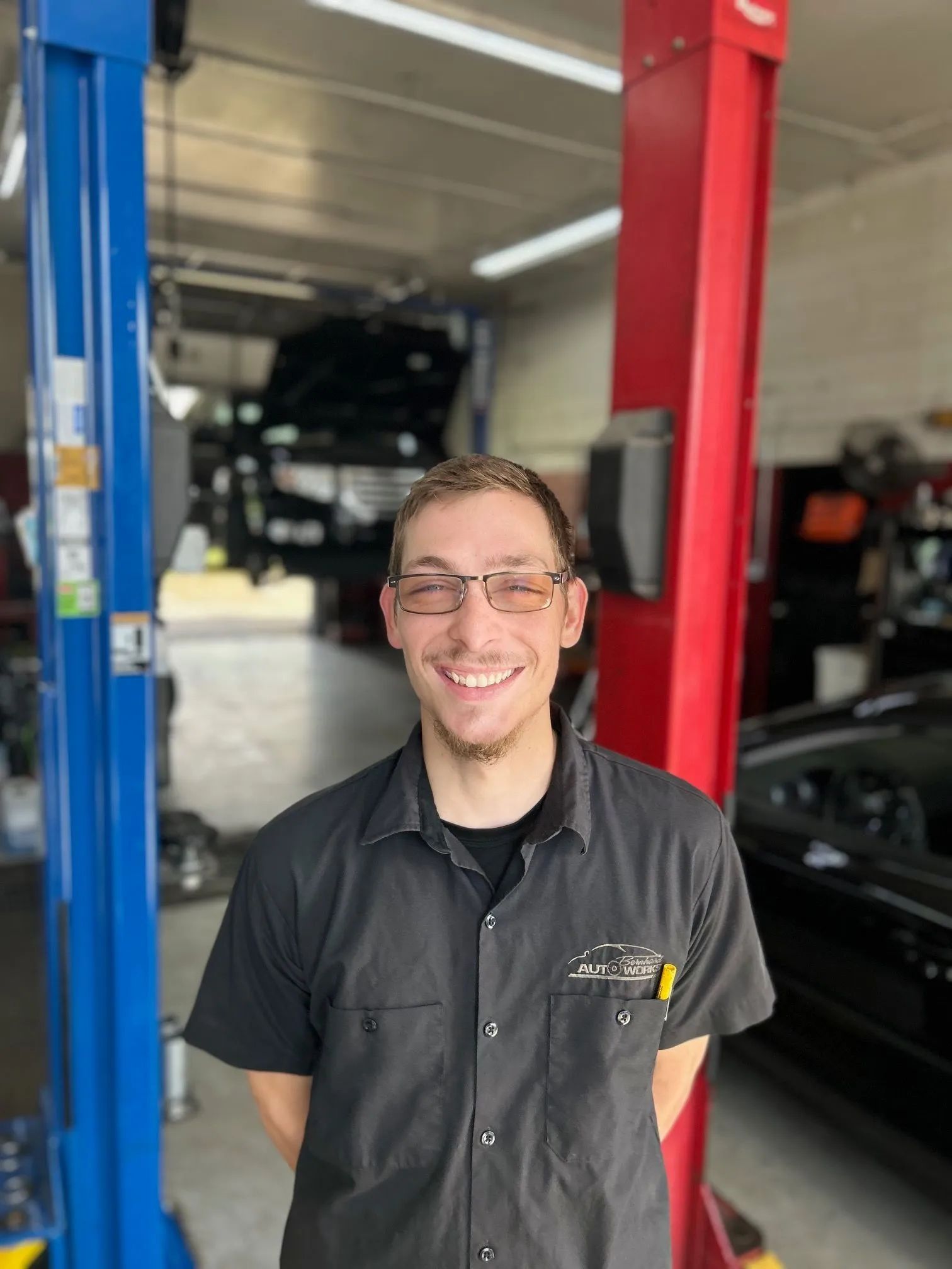 Smiling mechanic in a black shirt standing in an auto shop between blue and red car lifts