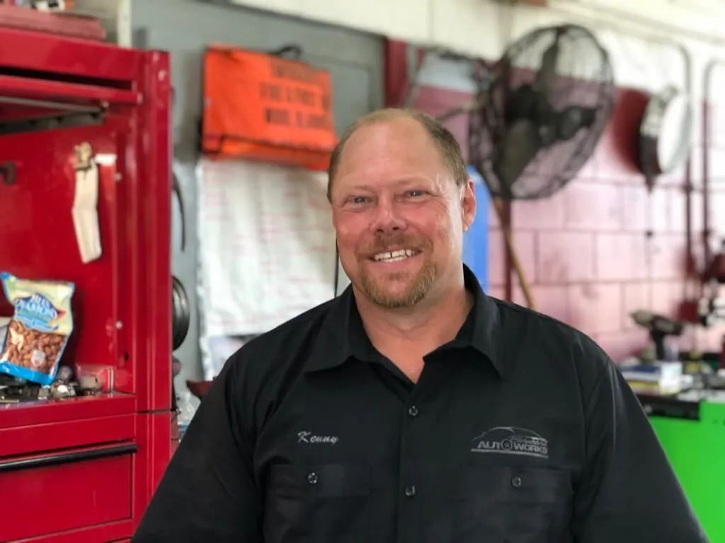 Smiling man in a black shirt standing in a red workshop beside a red tool cabinet