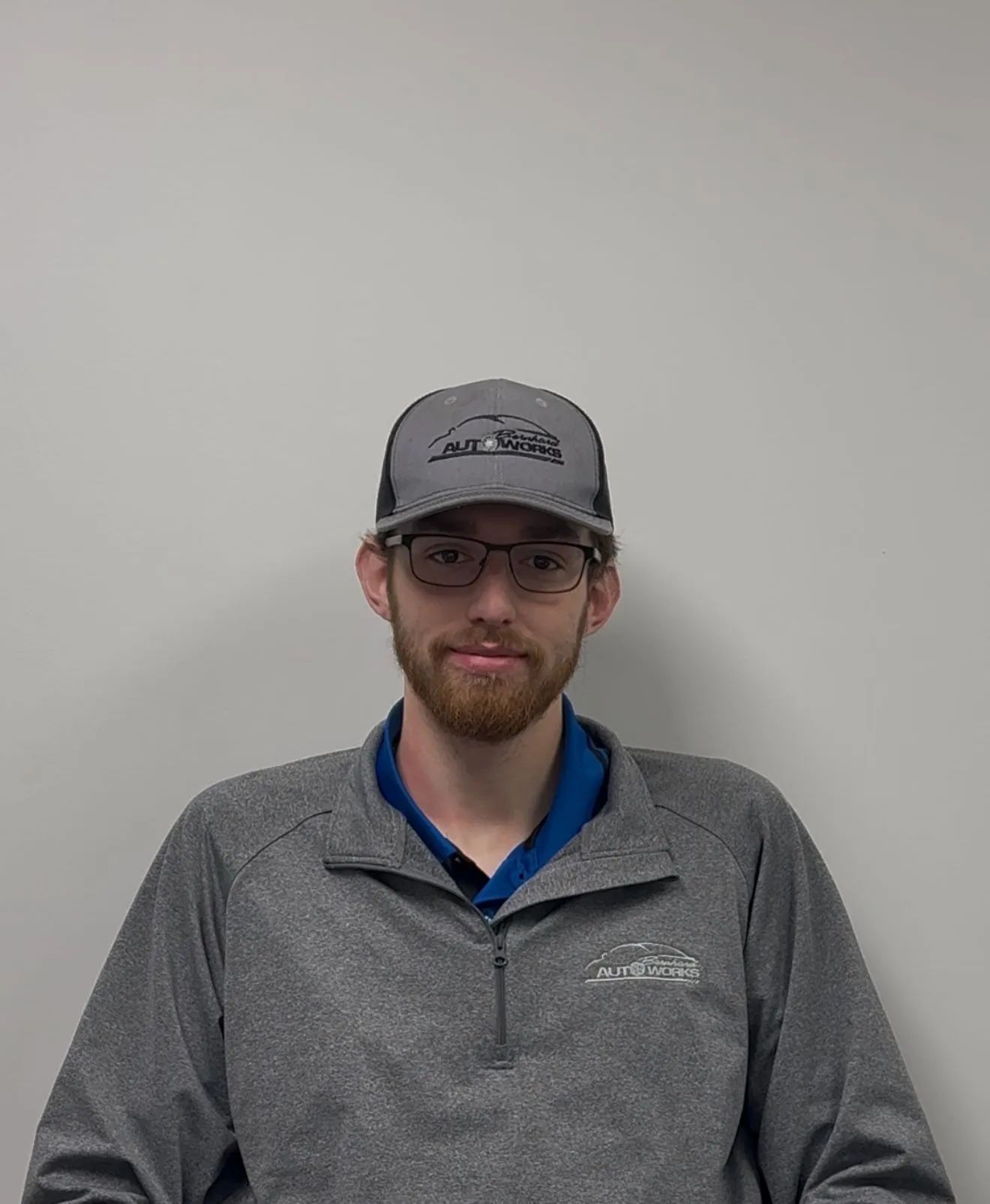 Person wearing a gray cap and sweater, sitting against a plain light wall.