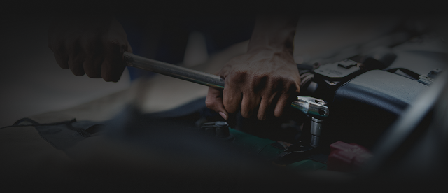 Hands using a wrench to work on a car engine in a dark garage
