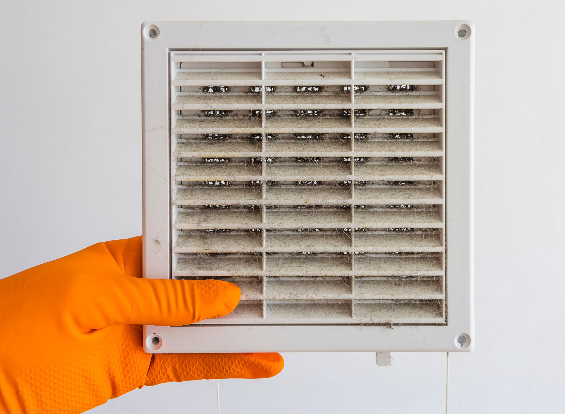 A person wearing orange gloves is holding a dirty air vent.
