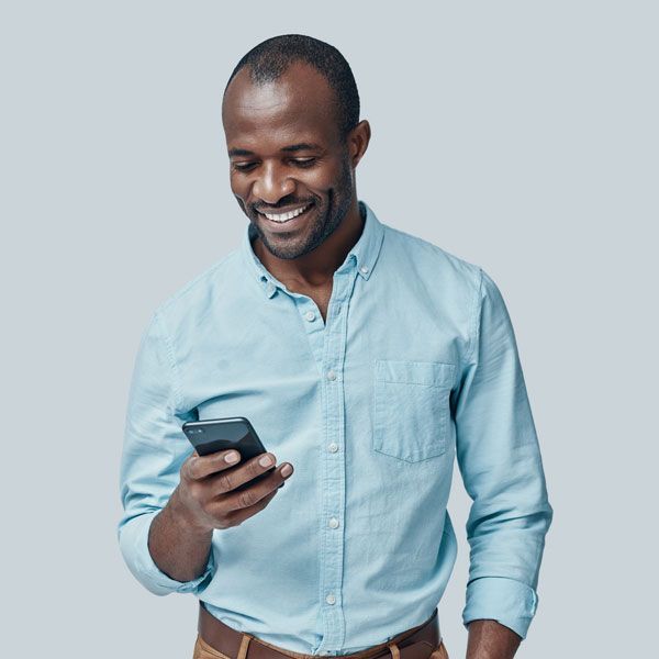 Smiling man in a light blue shirt looking at a smartphone against a plain gray background