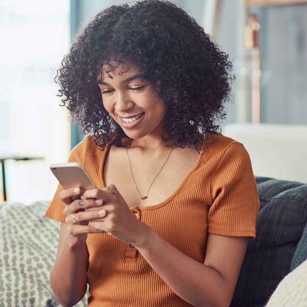 Smiling woman in an orange shirt reading a phone on a couch