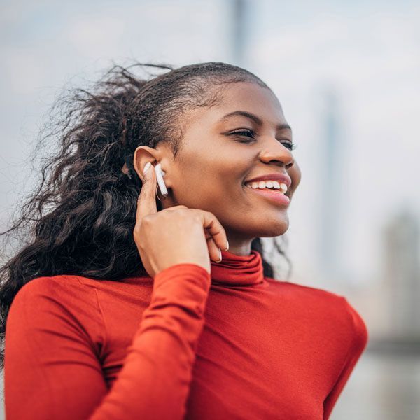 Smiling woman in a red turtleneck adjusting earbuds outdoors