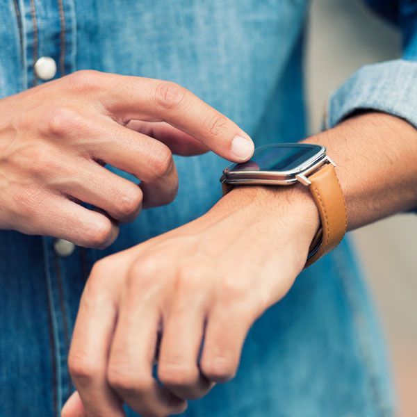 Hand using a smartwatch with a tan leather band, adjusting it on the wrist
