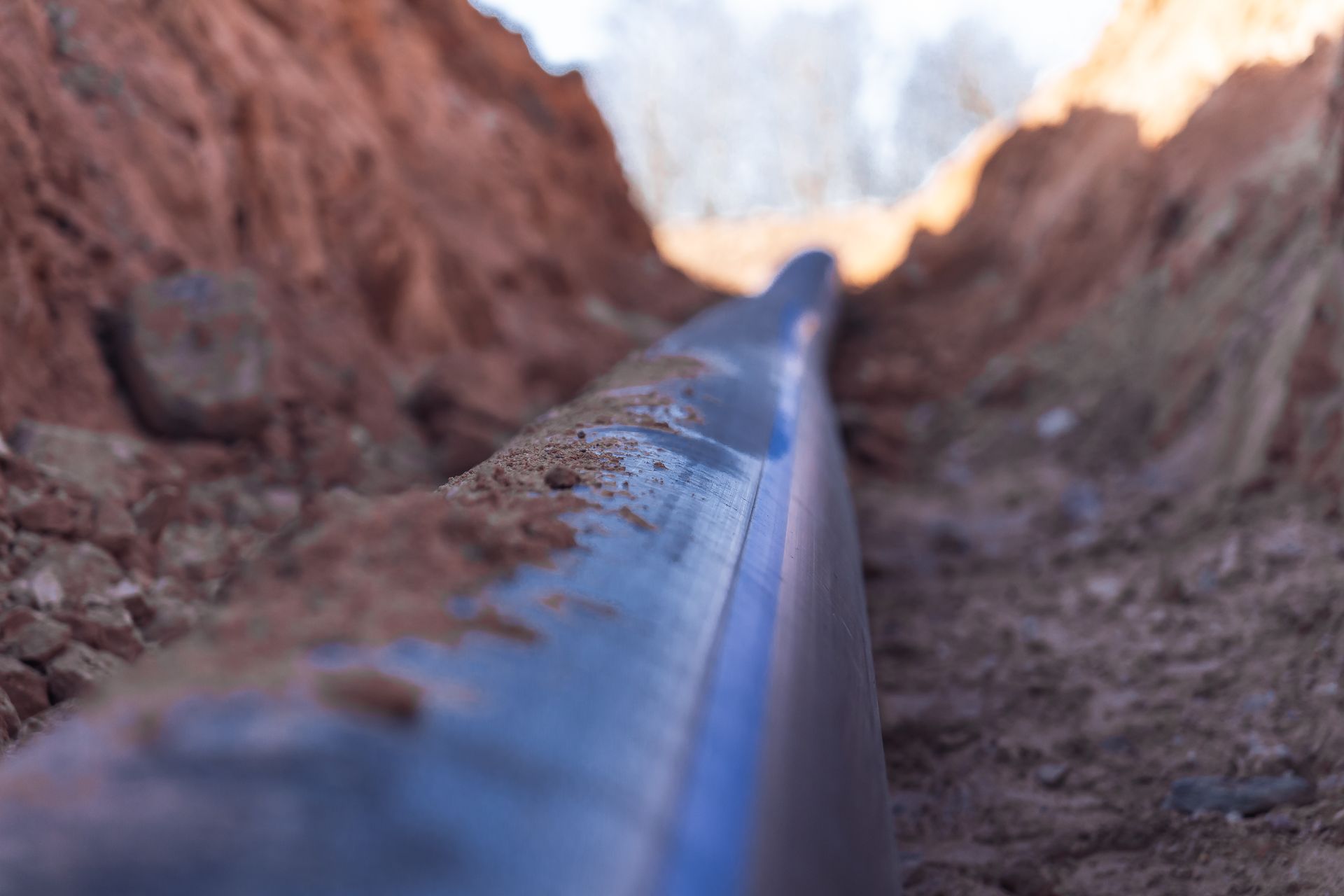 Close-up of a black pipe running through a muddy trench with blurred dirt walls on both sides